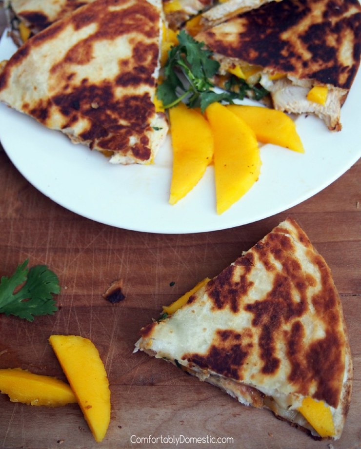 Wedges of chicken-mango-quesadillas-with-brie on a white plate and wooden cutting board. 