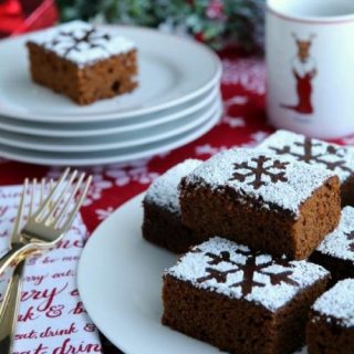 Plate of stacked gingerbread cake squares with stenciled powdered sugar snowflakes on top.