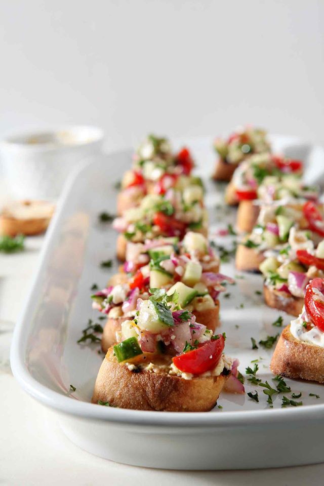 Rows of Greek bruschetta on a white platter.