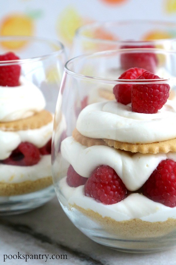 Two clear glasses of no bake lemon cheesecake parfaits on a white background.