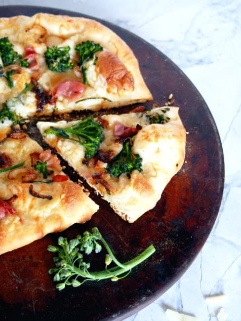 Prosciutto Broccolini Pizza proves that simple pizzeria style pizza is easily made at home! The chewy, thin crust pizza dough brushed with garlic butter, then topping it salty prosciutto, earthy broccolini, sweet caramelized onions, and shaved Asiago cheese is a taste to behold.